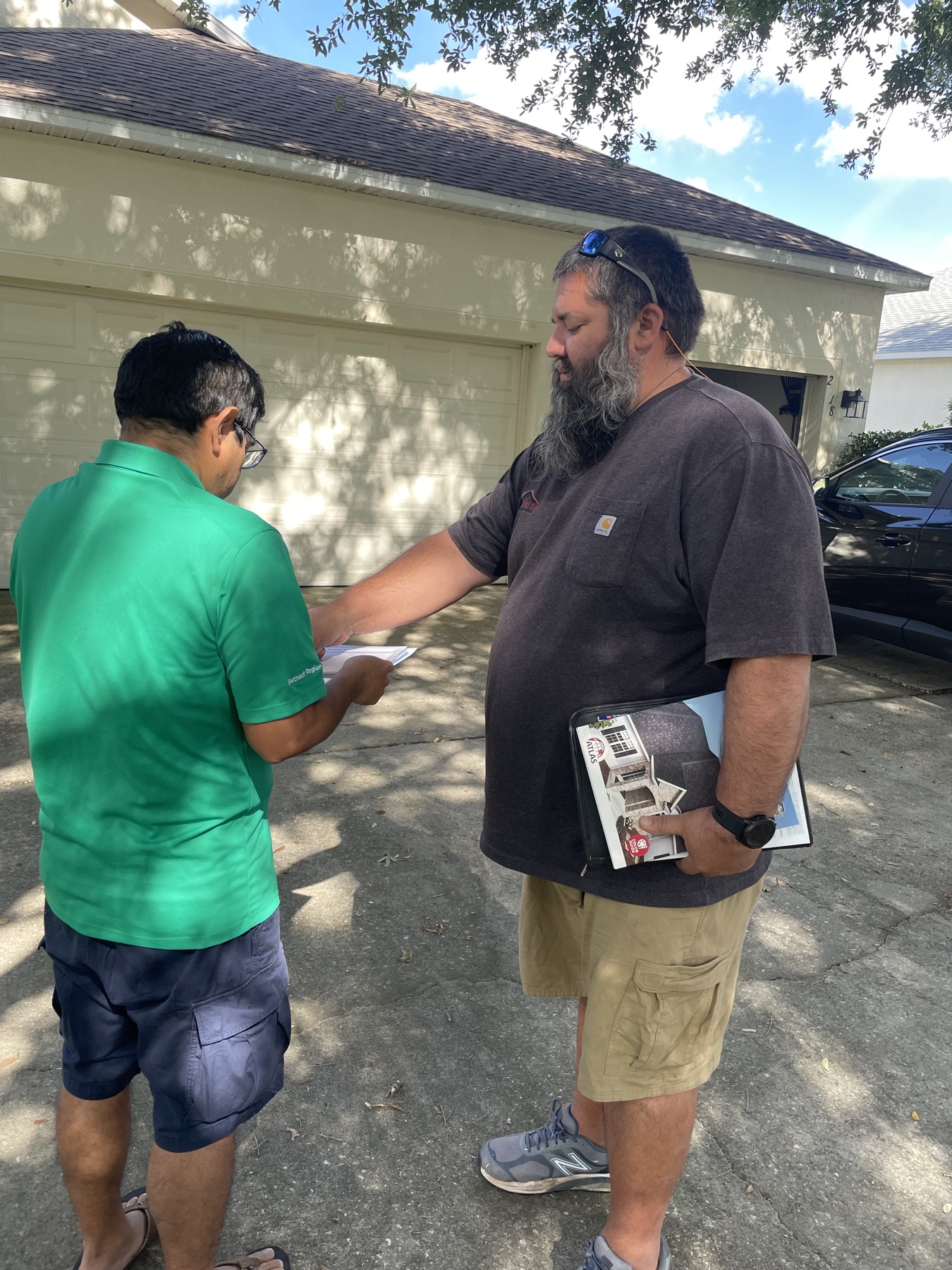 Erik consulting with a homeowner in their driveway, Atlas binder in hand